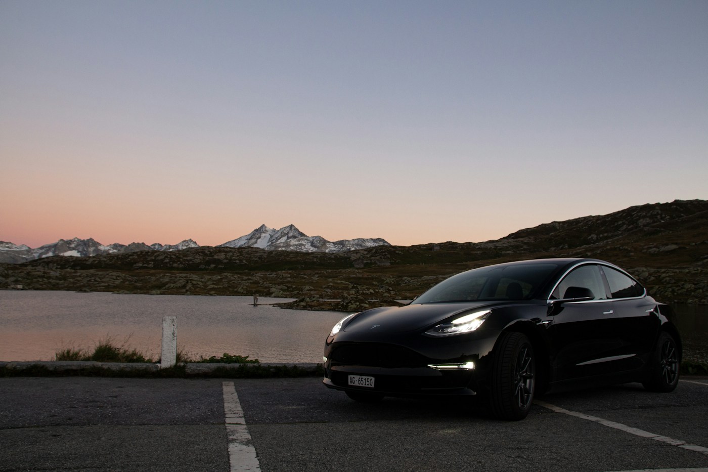 Tesla Model 3 negro junto a un lago al atardecer